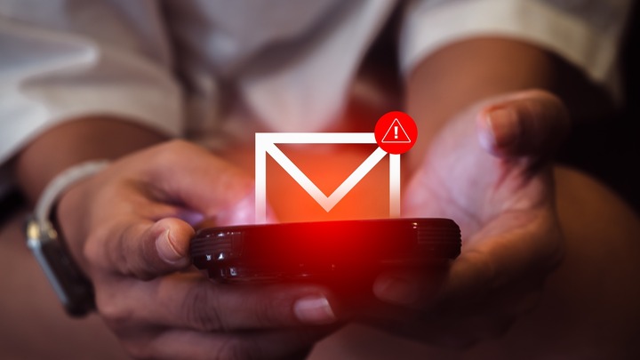 Zwei Hände halten ein Smartphone, über dem ein Mail-Symbol mit Warnhinweis schwebt