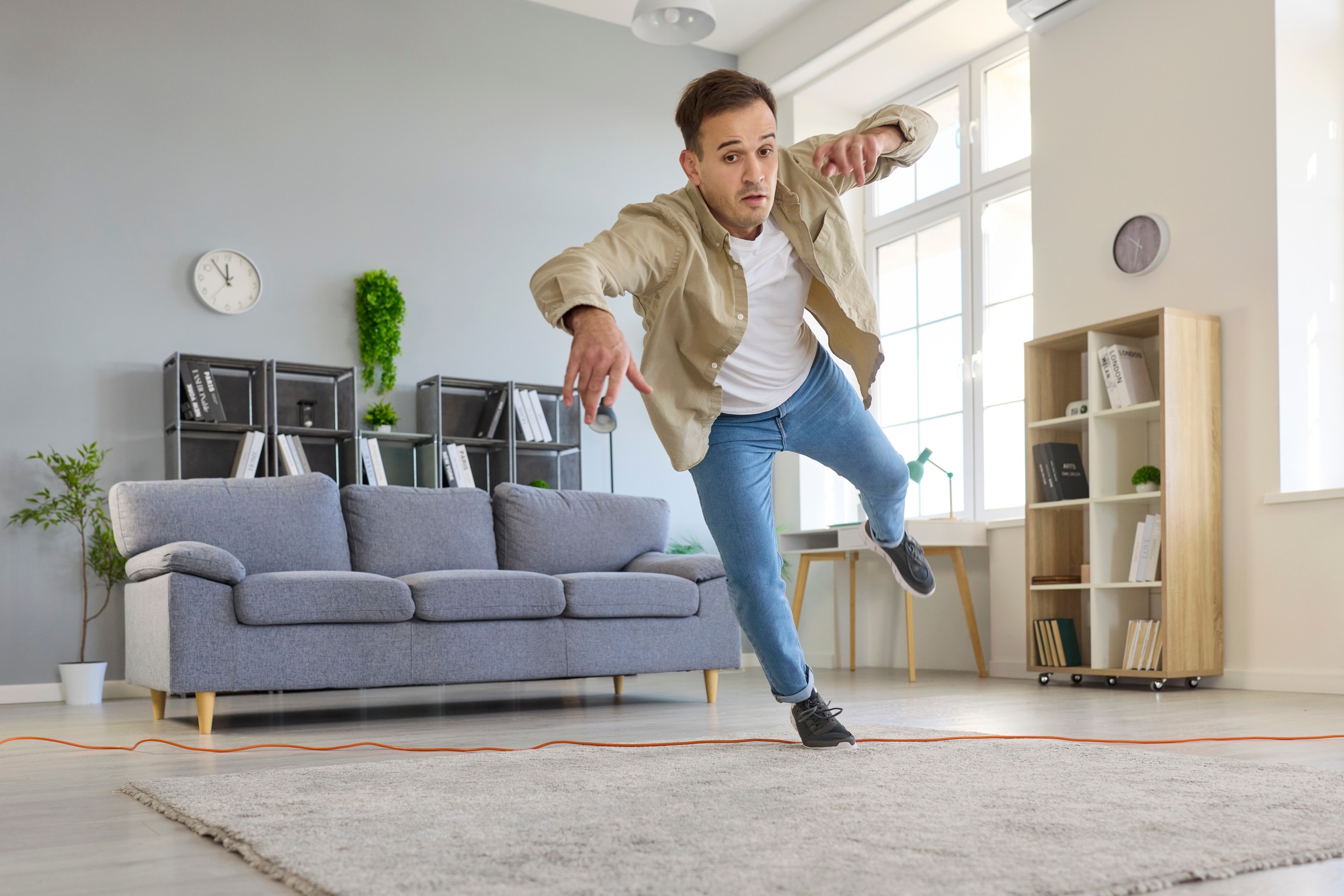Das Bild zeigt einen Mann der im Wohnzimmer vor seinem Sofa ausrutscht und hinfällt. 